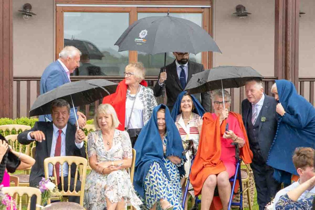 Wedding guests using umbrellas to stay dry during an outdoor wedding