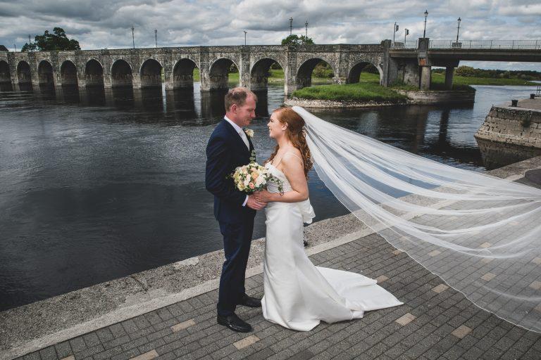 The bride holding the grooms hands, standing in front of the stone bridge posing for a wedding photo at Shannonbridge.
