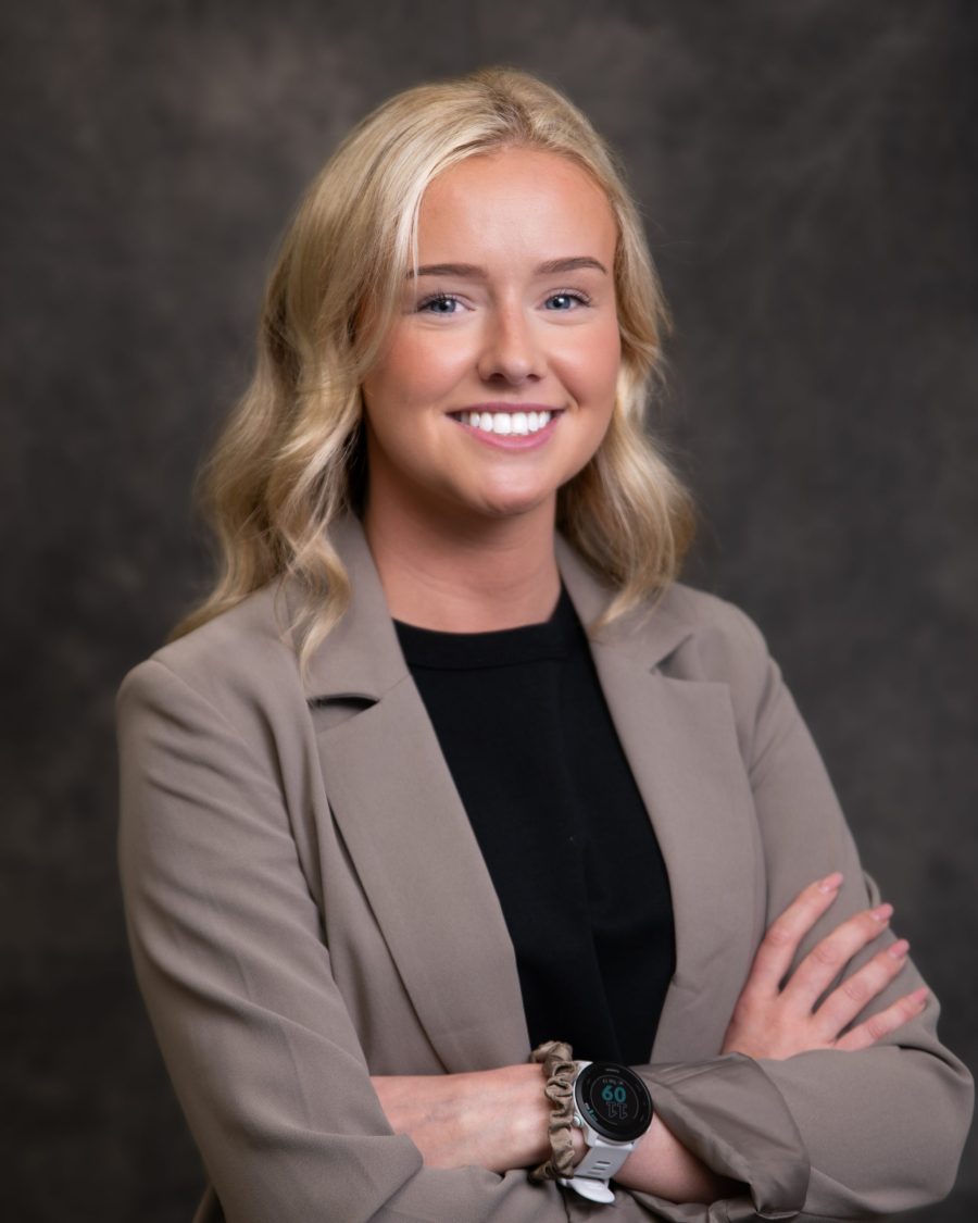 Corporate headshot of a woman in a cream blazer on a grey background