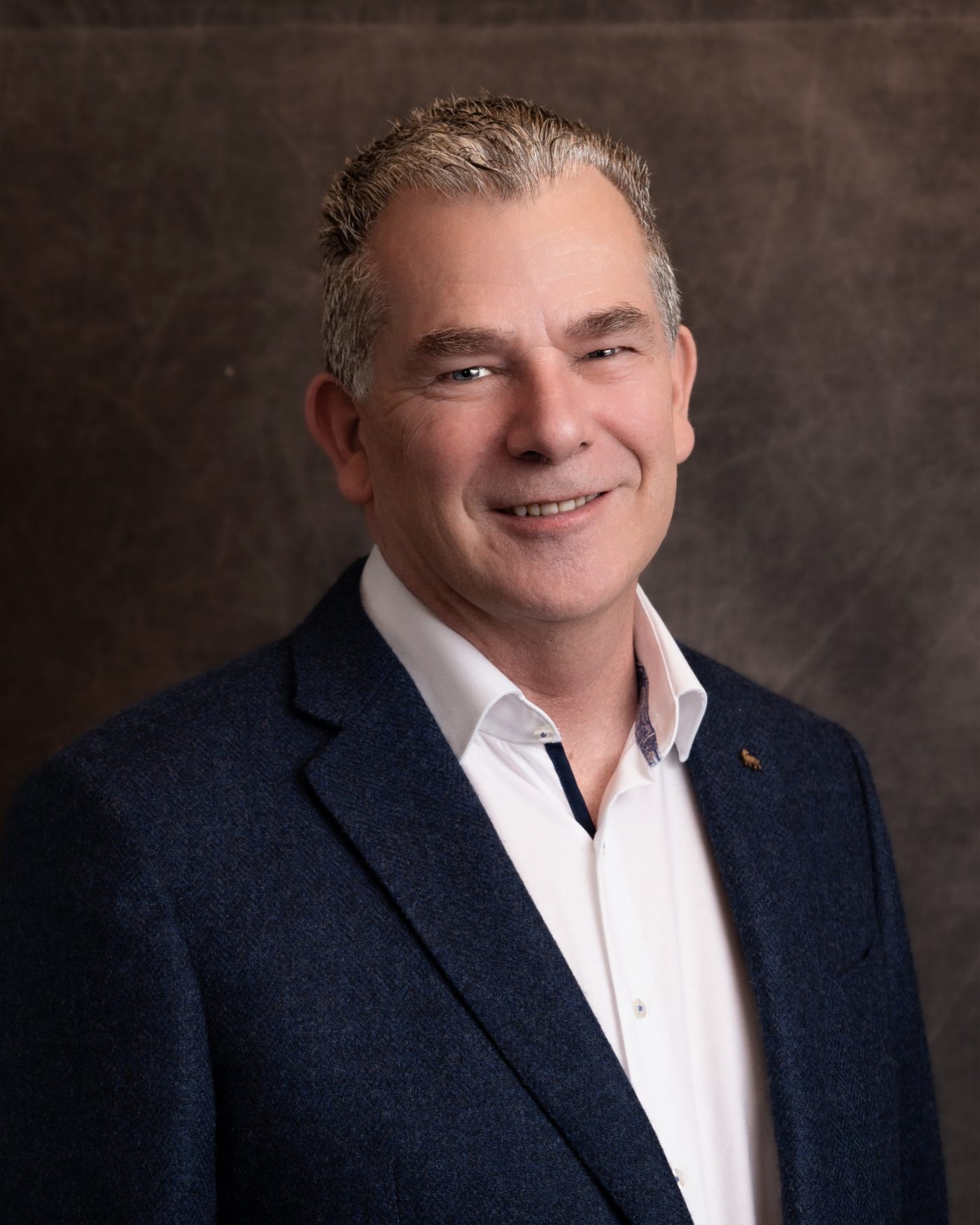 Business portrait of a man in a navy tweed blazer and white shirt on a textured brown backdrop