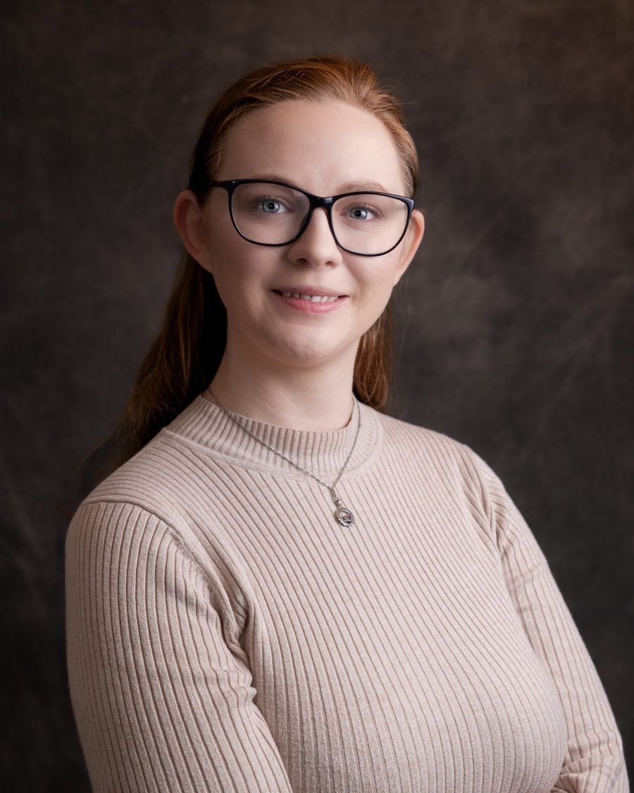 Professional headshot of a woman wearing glasses and a ribbed jumper