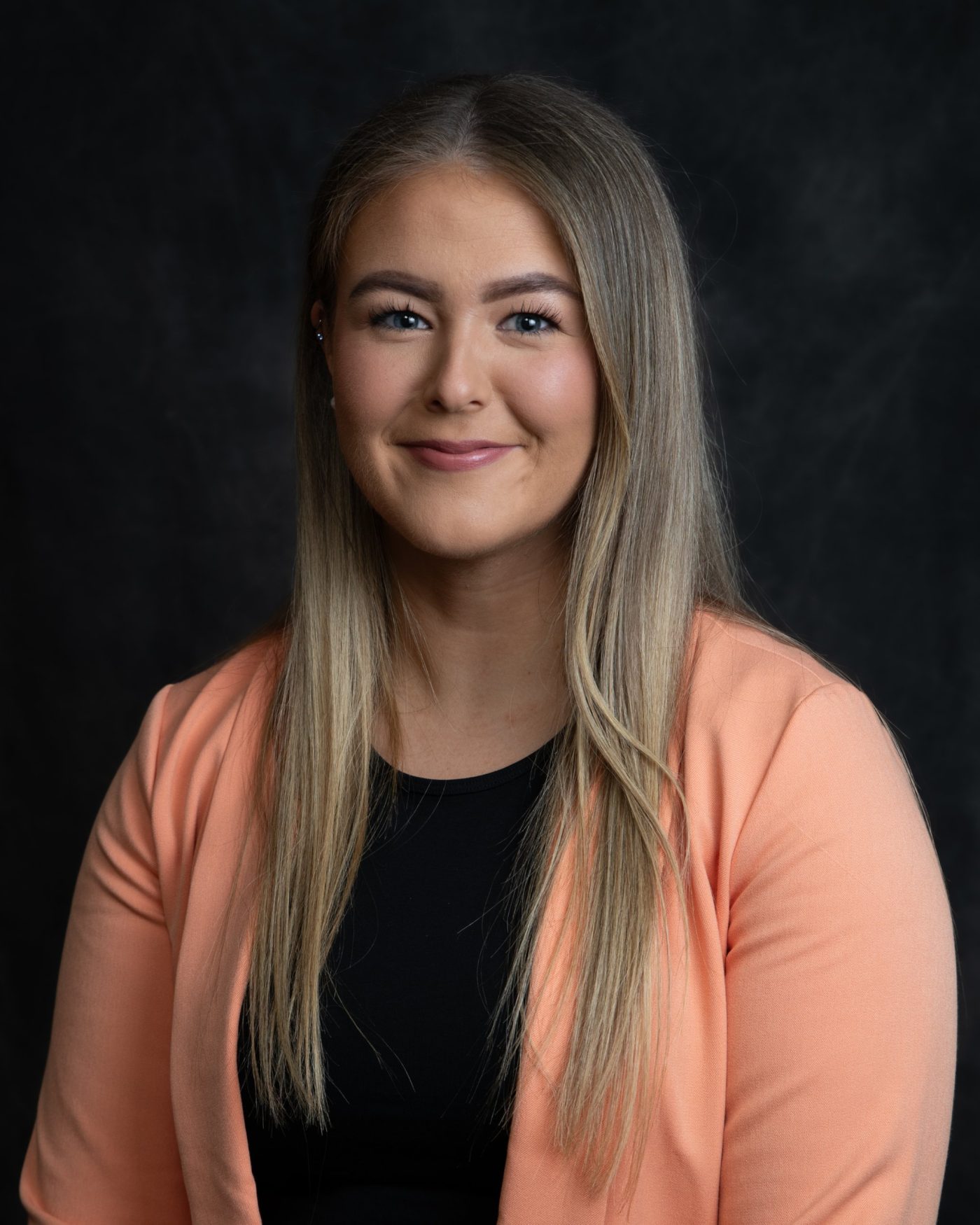 Headshot of a woman with long hair in a peach blazer on a black backdrop