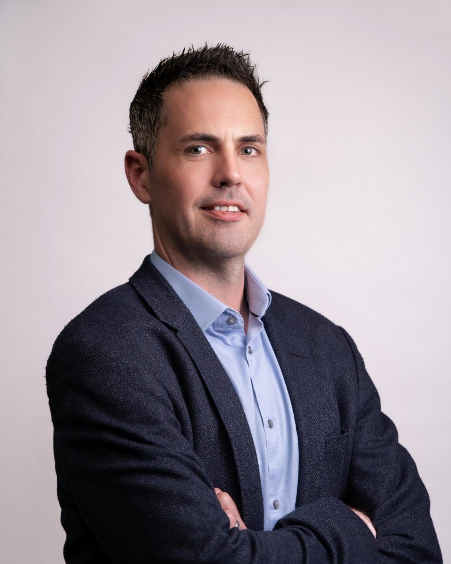 Business portrait of a man in a navy blazer with arms folded on a light backdrop