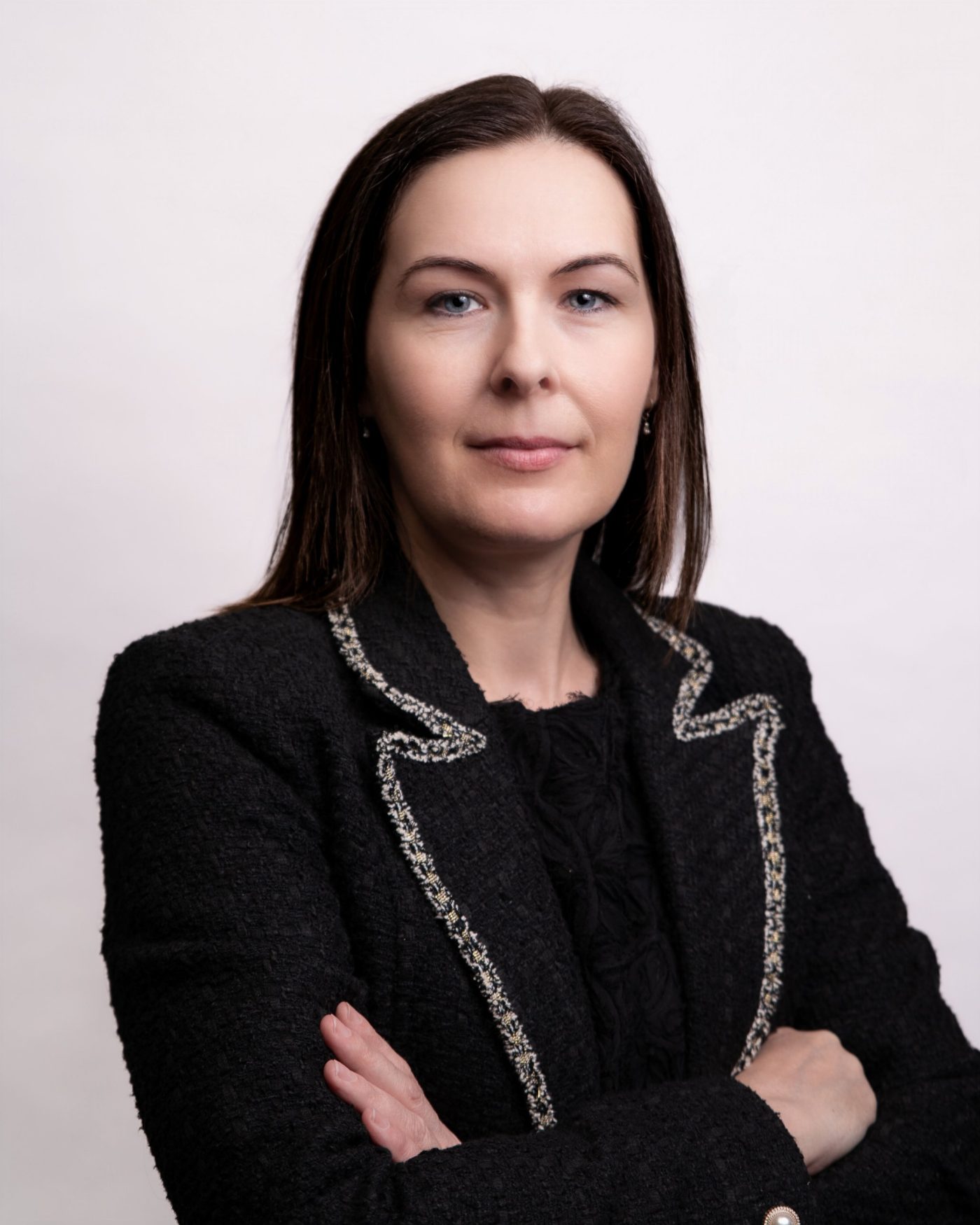 Executive portrait of a woman in a black tailored jacket with arms folded on white